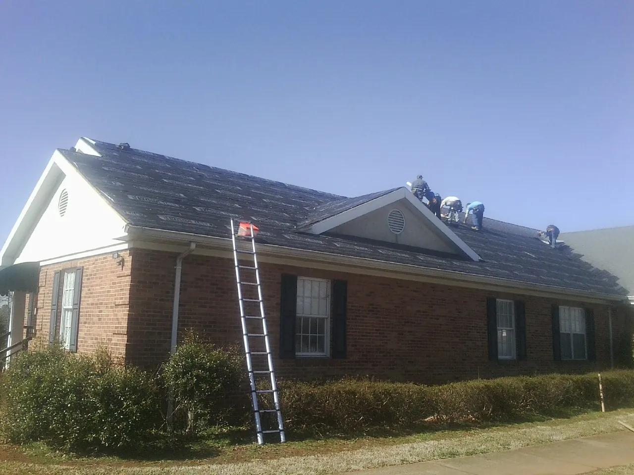 Crew tearing shingles off a brick ranch roof with a ladder set — Emergency Roof Repair work by our crew in Grantville